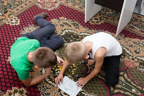 Two young boys are on a patterned rug, deeply engaged in constructing with co Stock Photos