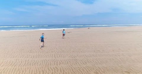 Two young boys running towards mother sitting on empty beach smooth dolly Stock Footage 87574121
