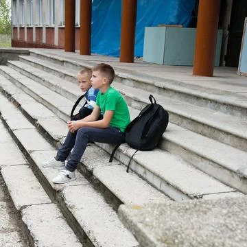 Two young boys sitting thoughtfully on outdoor concrete steps. Backpack nea.. Stock Photos
