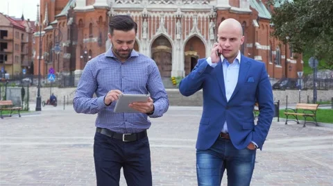 Two young businessmen are walking while using tablet pc and mobile phone Stock Footage