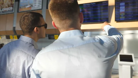 Two young businessmen looking at flight schedule at airport. Business man Stock Footage 229292743