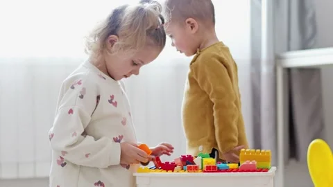 Two young children are engaged in playtime with colorful building blocks. They Stockbeeldmateriaal 336460241
