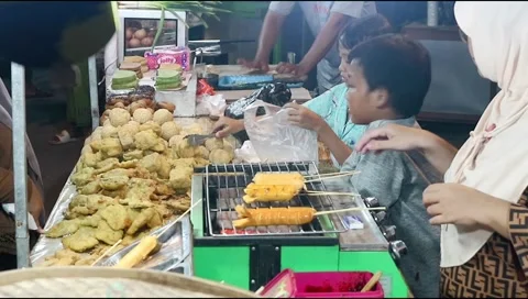 Two young children help their mother serve customers at the night market Stock Footage 302773365