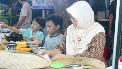 Two young children help their mother serve customers at the night market Stock Footage 302773367