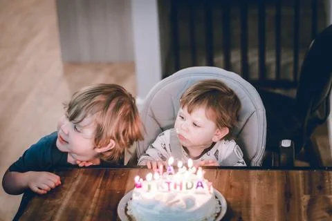 Two young children leaning over a birthday cake with lit candles, preparing.. Stock Photos