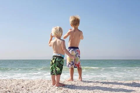 Two young children looking out over ocean on beach Stock Photos