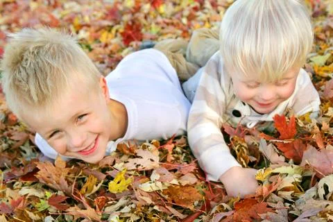 Two young children playing in fall leaf pile Stock Photos