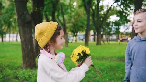 Two young children playing in a lively park on a sunny day, with a boy handing a Stock Footage 313751127