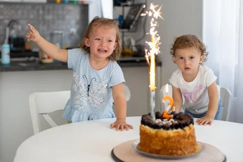 Two young children react to a birthday cake with sparklers. One girl looks .. Stock-Fotos