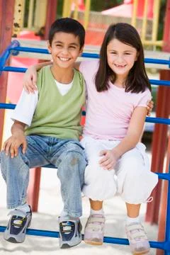 Two young children sitting on playground structure smiling (selective focus) Stock Photos