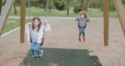 Two young children swing on playground swings, the little girl is singing Stock-Footage 115970321