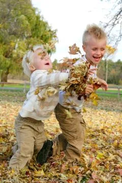 Two young children throwing fall leaves outside Stock Photos