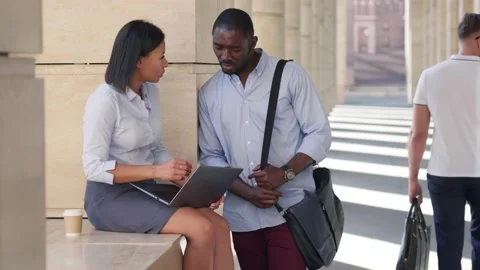 Two young colleagues using laptop and discussing online work together outdoors Stock Footage 157380620
