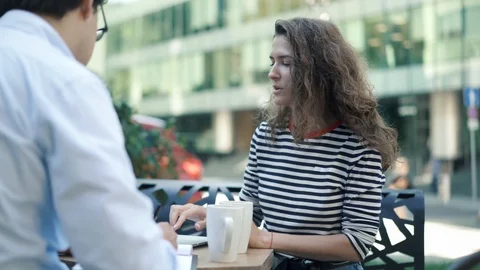 Two young colleagues working in summer caffe with laptop and clipboard 스톡 동영상 96997062