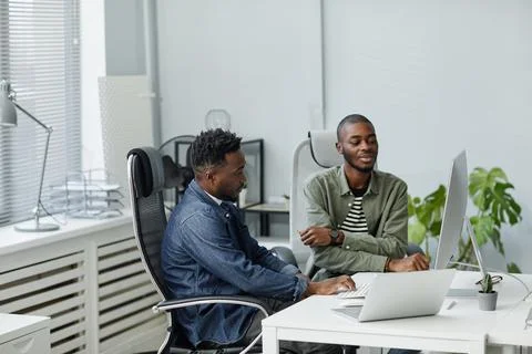 Two young confident programmers sitting by desk in front of computer monitor Stockfoto's