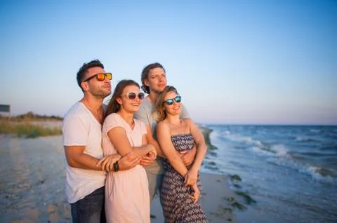 Two young couples admire a sunset on the sea coast. Stock Photos