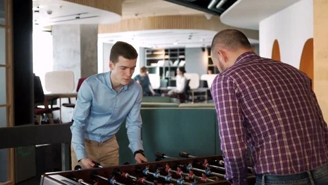 Two young coworkers play table football game to relax and have rest during busy Stock Footage 80083501