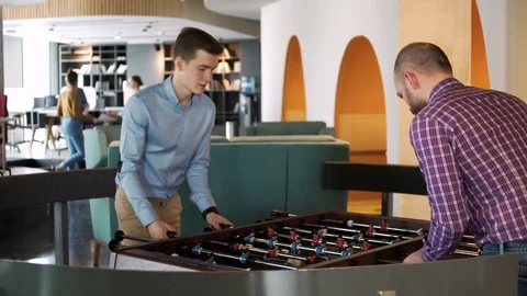 Two young coworkers play table football game to relax and have rest during busy Stock Footage 80083679