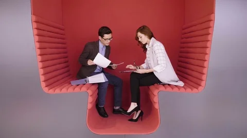 Two young coworkers talking about business tasks sitting in modern red zone for Stock Footage 80923819