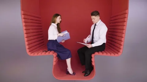 Two young coworkers talking about business tasks sitting in modern red zone for Stock Footage 80938187