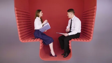 Two young coworkers talking about business tasks sitting in modern red zone for Stock Footage 80938620