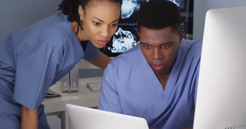 Two young doctors working together on multiple computers Stockbeeldmateriaal 42670709