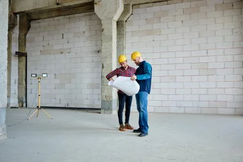 Two young engineers or builders in hardhats and casualwear looking at blueprint Stock Photos