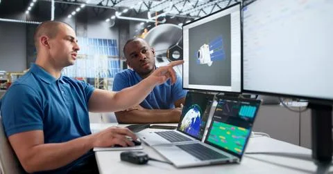 Two Young Engineers Use Computer Software To Design Solar Satellite. Stock Photos