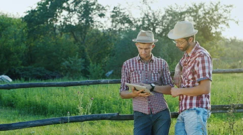 Two young farmer standing by a fence in the countryside, chatting, enjoying Stockbeeldmateriaal 65454242