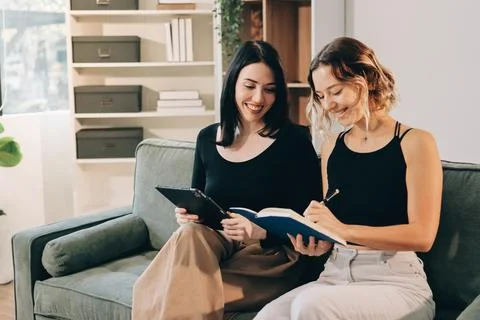 Two young female students using a laptop while sitting on a sofa at home. S.. Stockfoto's