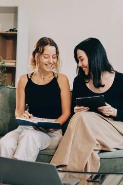Two young female students using a laptop while sitting on a sofa at home. S.. Stockfoto's