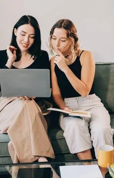 Two young female students using a laptop while sitting on a sofa at home. S.. Stockfoto's