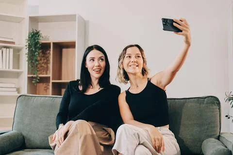 Two young female students using a laptop while sitting on a sofa at home. S.. Stockfoto's