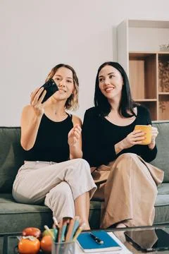 Two young female students using a laptop while sitting on a sofa at home. S.. Stockfoto's