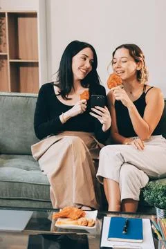 Two young female students using a laptop while sitting on a sofa at home. S.. Stockfoto's