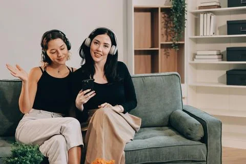 Two young female students using a laptop while sitting on a sofa at home. S.. Stockfoto's