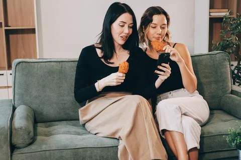 Two young female students using a laptop while sitting on a sofa at home. S.. Stockfoto's
