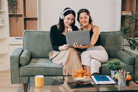 Two young female students using a laptop while sitting on a sofa at home. S.. Stockfoto's