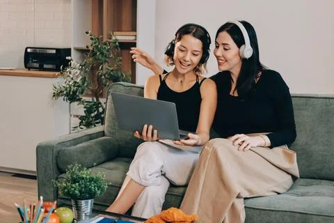 Two young female students using a laptop while sitting on a sofa at home. S.. Stockfoto's