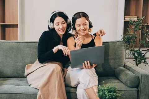 Two young female students using a laptop while sitting on a sofa at home. S.. Stockfoto's