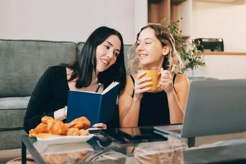 Two young female students using a laptop while sitting on a sofa at home. S.. Stockfoto's
