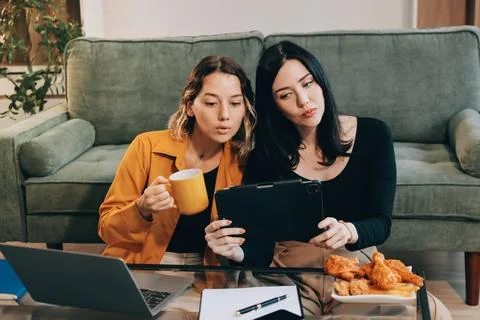 Two young female students using a laptop while sitting on a sofa at home. S.. Stockfoto's