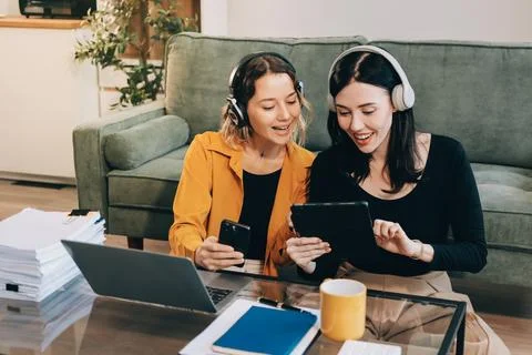 Two young female students using a laptop while sitting on a sofa at home. S.. Stockfoto's