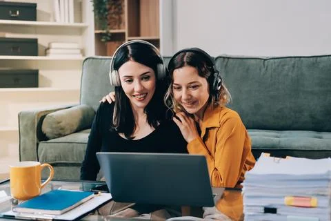 Two young female students using a laptop while sitting on a sofa at home. S.. Stockfoto's