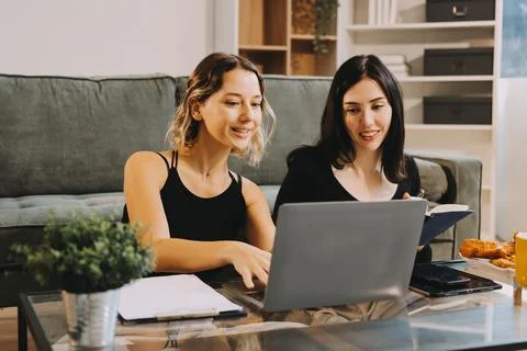 Two young female students using a laptop while sitting on a sofa at home. S.. Stock Photos