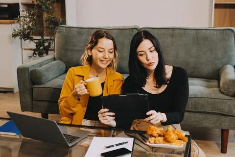 Two young female students using a laptop while sitting on a sofa at home. S.. Stock Photos