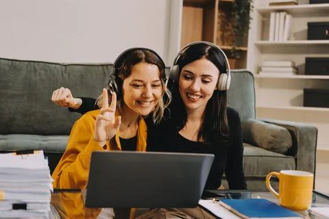 Two young female students using a laptop while sitting on a sofa at home. S.. 库存照片