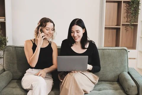 Two young female students using a laptop while sitting on a sofa at home. S.. Stock Photos