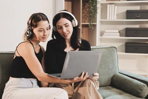Two young female students using a laptop while sitting on a sofa at home. S.. Stock Photos