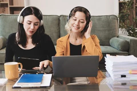 Two young female students using a laptop while sitting on a sofa at home. S.. Stock Photos